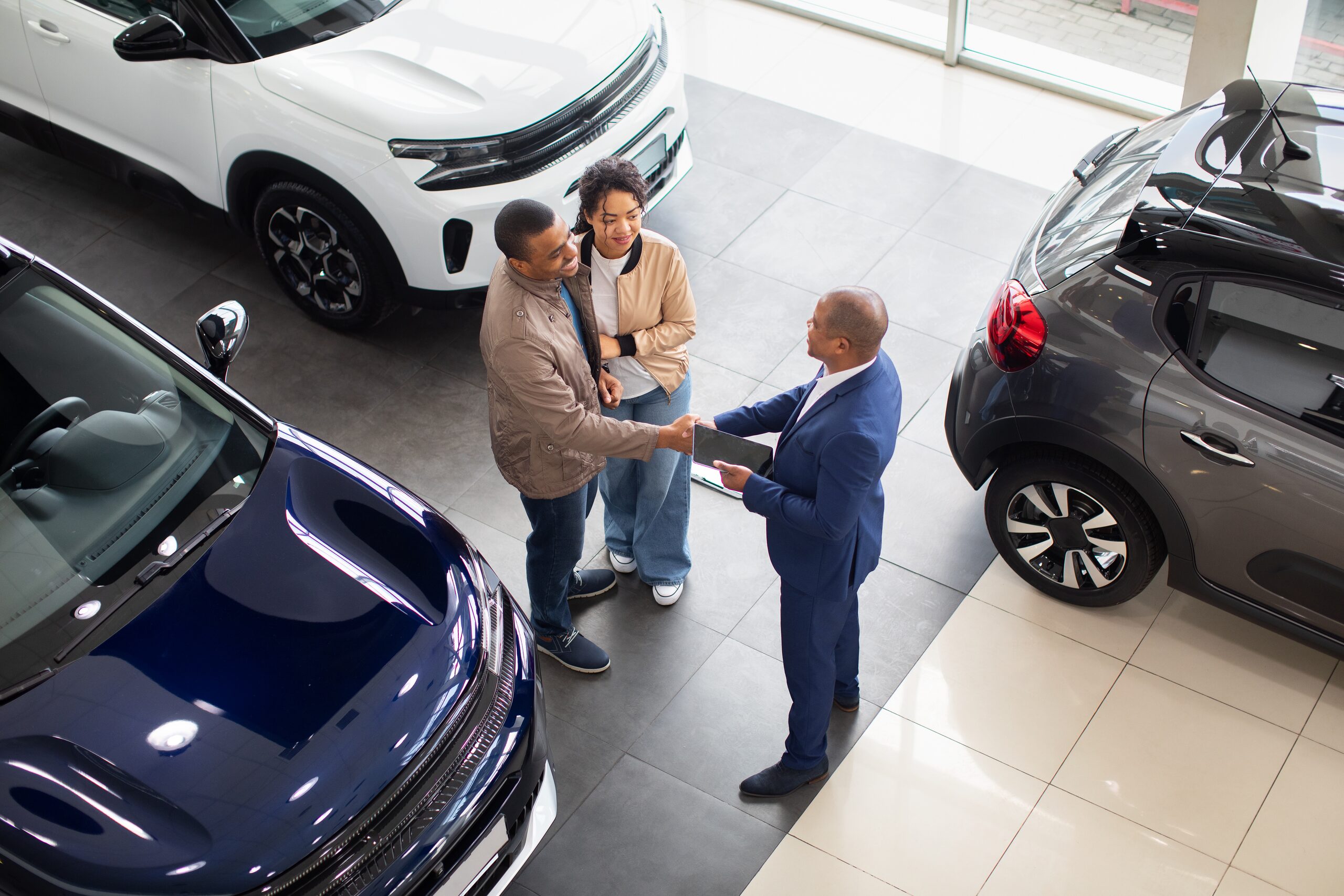 A salesperson shakes hands with a smiling couple on a dealership showroom floor