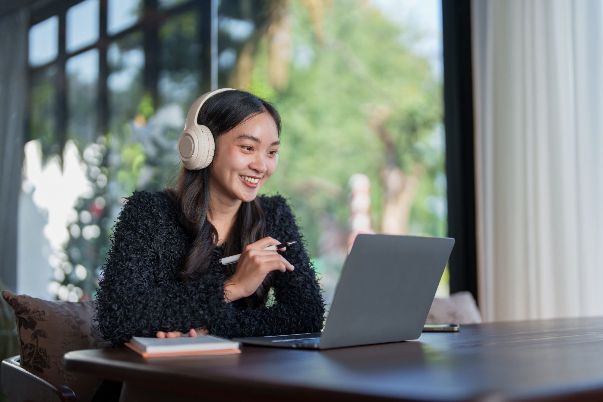 An advisor in headphones smiles as she reviews her own interview on her laptop