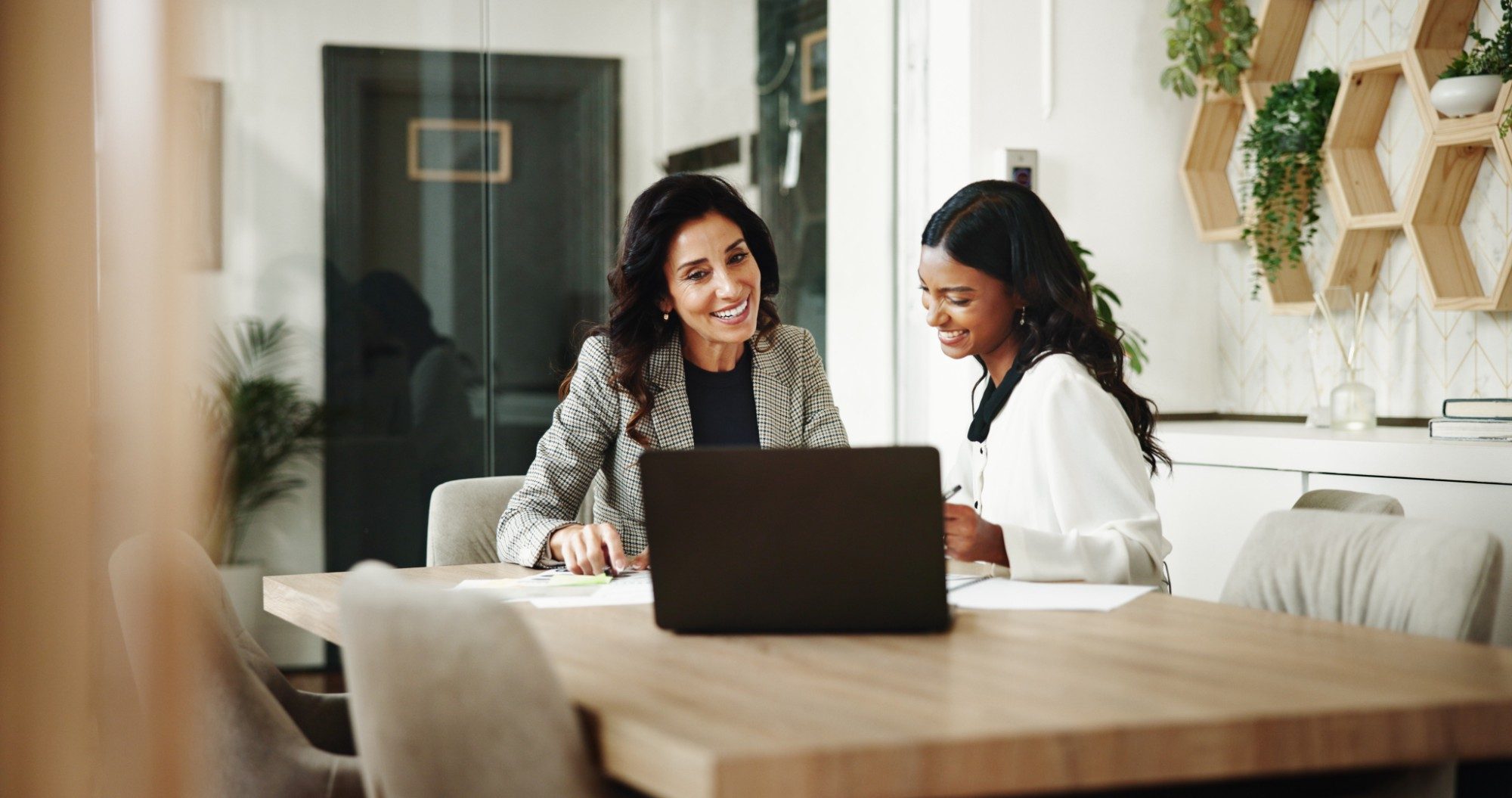 An advisor and a colleague smile over a laptop at a meeting table