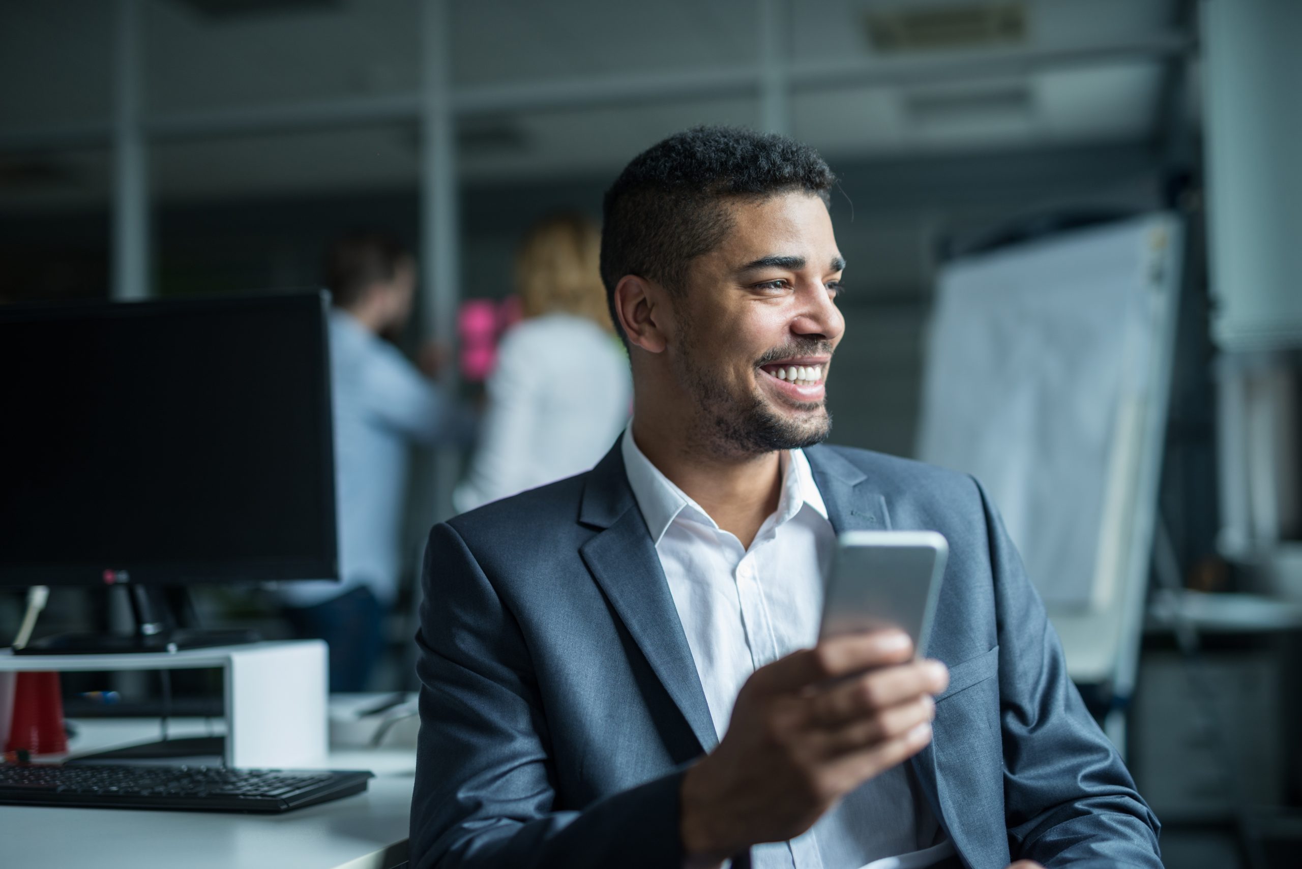 An advisor smiles at his phone at his desk in an open office