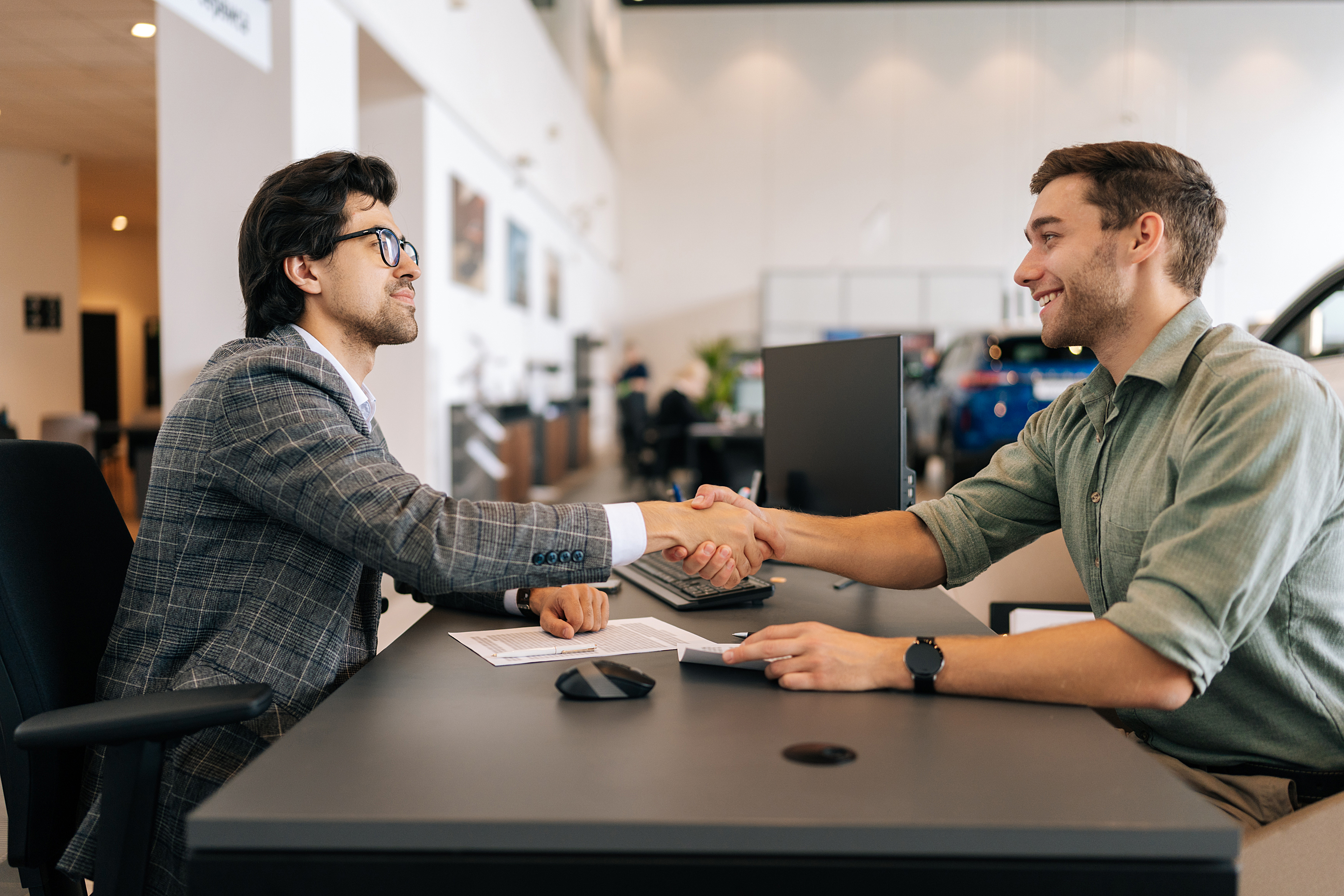 A customer and a sales consultant shake hands across a desk