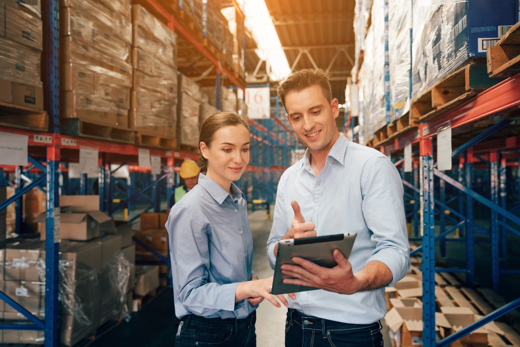 A territory rep shows a distributor's manager coaching notes on a tablet in a warehouse aisle