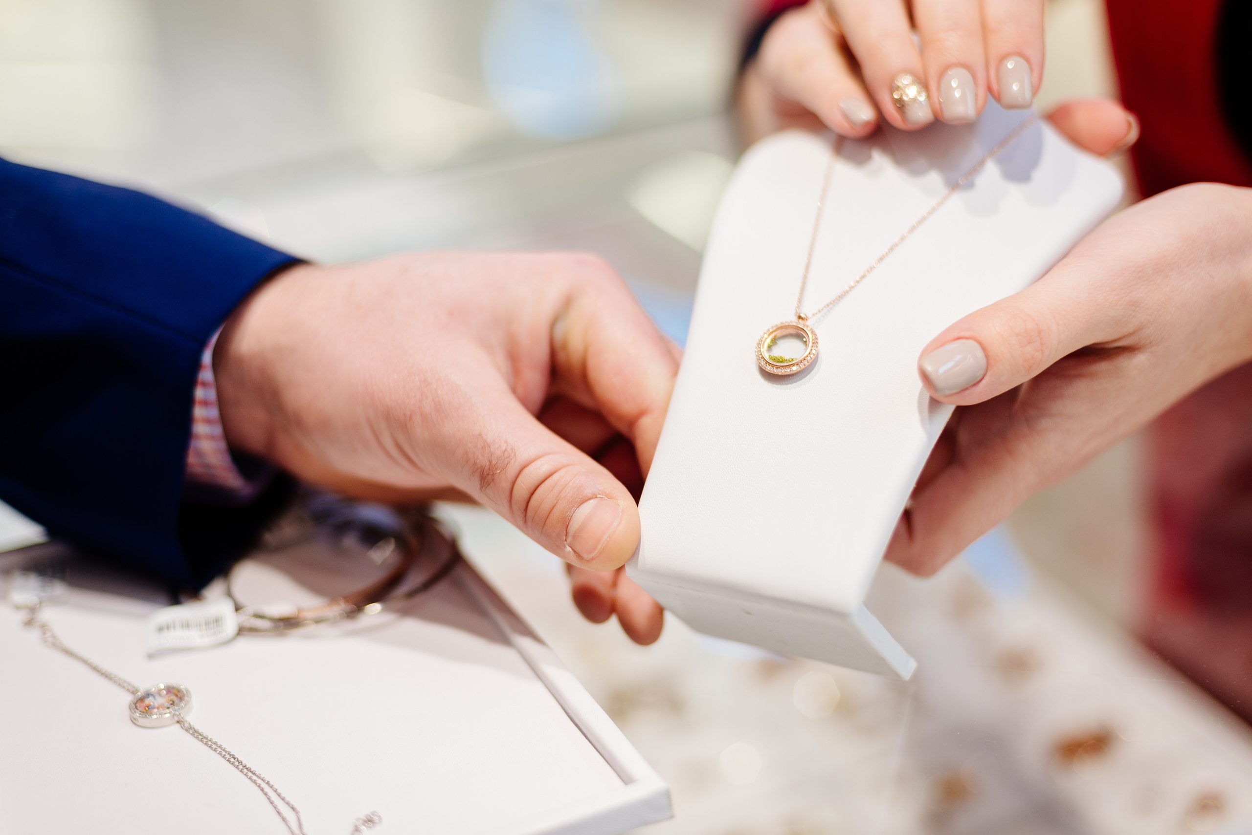 A seller presents a gold pendant necklace to a customer across a jewelry counter